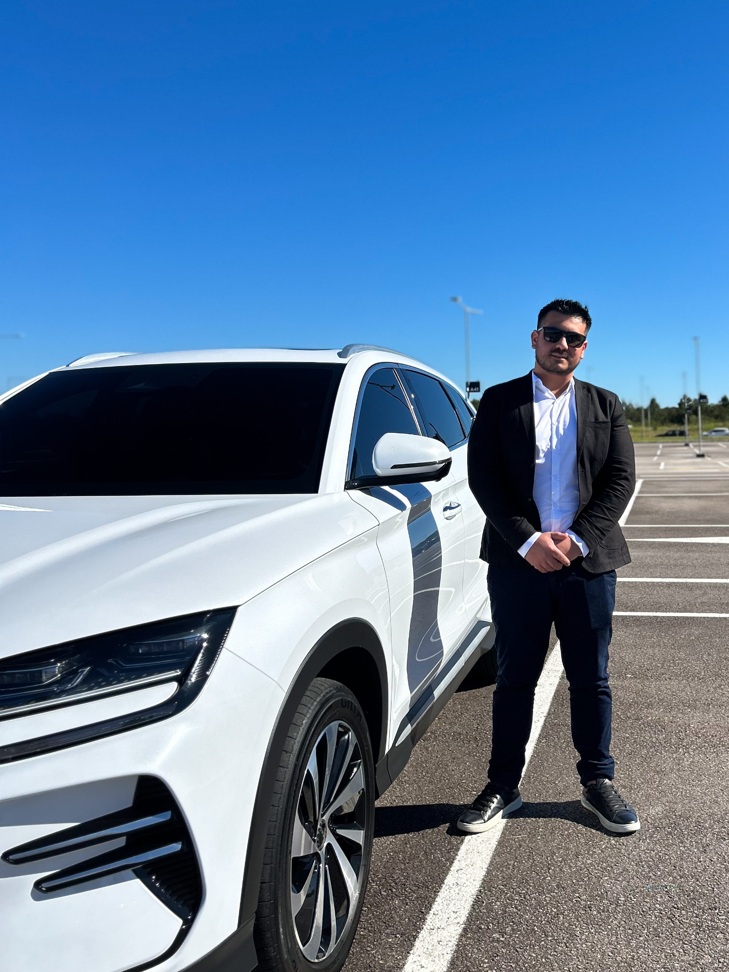 Motorista da Douglas Transfer ao lado do SUV branco no estacionamento do Floripa Airport